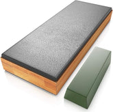 The leather strop sharpener features a double-sided design with a textured black surface on one side and a smooth, wooden base. A green honing compound block is positioned next to the sharpener.