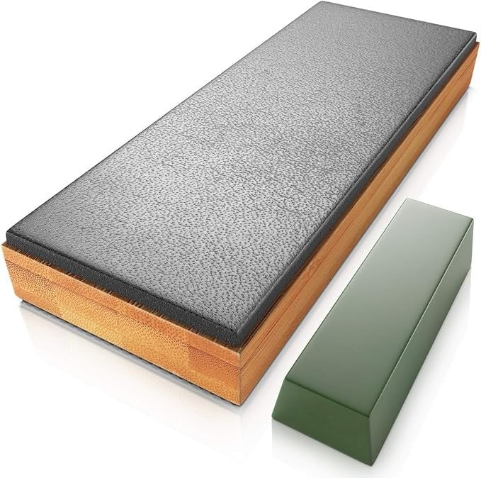 The leather strop sharpener features a double-sided design with a textured black surface on one side and a smooth, wooden base. A green honing compound block is positioned next to the sharpener.