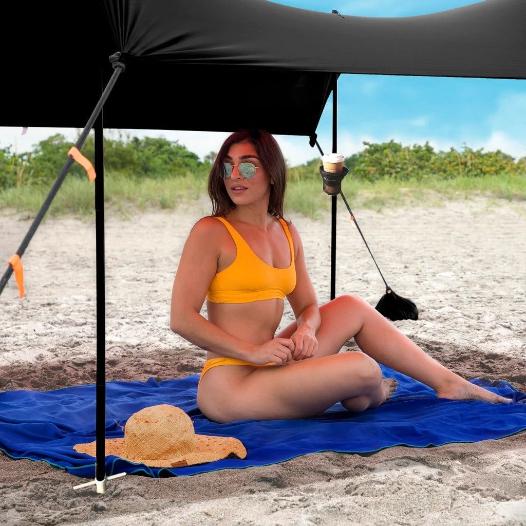 Close-up of a black support pole with a chain running alongside an attached fabric cover, situated on a grassy area. The arrangement illustrates the structure and stability features of the beach tent.