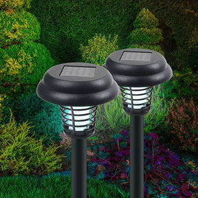 Two solar-powered bug zapper stakes feature a black dome top and a clear light shade, set against a vibrant garden background with various plants. The stakes are designed to provide illumination and attract insects.
