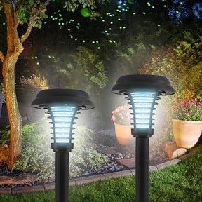 Two solar-powered bug zapper stakes are illuminated in a nighttime garden setting, featuring a sleek black design with a translucent, ribbed light cover. The stakes are positioned among greenery and flower pots, emphasizing their outdoor use.