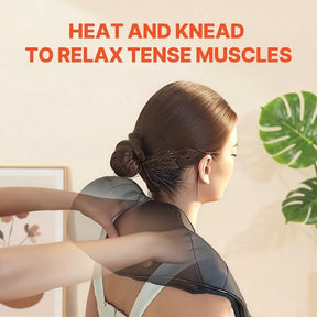 A person with their hair in a bun is wearing a neck and shoulder massager, while someone is gently placing the massager around their neck. The background features greenery and a wall decoration.