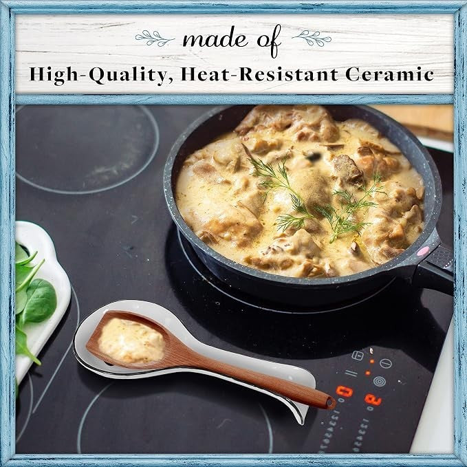White ceramic spoon rest with a curved shape featuring a wooden handle, positioned next to a cast iron skillet filled with a creamy dish, set on a modern cooktop with a sleek design, accompanied by greens on a plate.