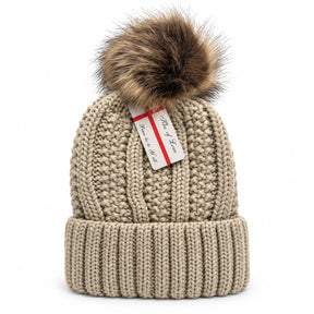 Knit beanie hat in a light beige color featuring a fluffy brown pom pom on top and a ribbed cuff at the base, showcasing a textured cable knit design.