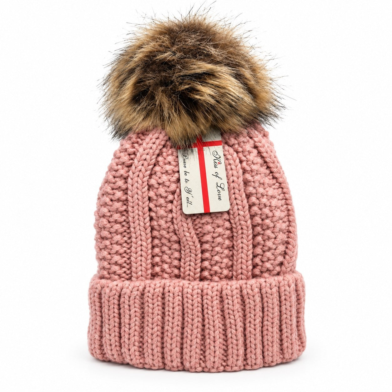 Soft pink knitted beanie featuring a large faux fur pom pom on top and a cozy fleece lining, with a ribbed cuff at the base. A small tag with "Kiss of Love" is attached near the top.