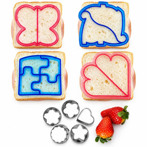 Four sandwich bread cutters in various shapes, including a butterfly, dinosaur, puzzle piece, and heart, atop slices of bread, with a set of five metal veggie and fruit cutters and two strawberries displayed at the bottom.