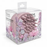 Pink scalp massager featuring soft, rounded bristles housed in a transparent box adorned with floral designs. The packaging highlights the product name and its purpose for scalp exfoliation and stimulation.