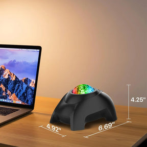 The Rossetta Star Projector features a black, rounded base with a colorful, illuminated dome showcasing red, green, and blue patterns at the top, positioned next to a laptop on a wooden surface. Dimensions are indicated as 4.25 inches in height, 6.69 inches in width, and 4.92 inches in depth.