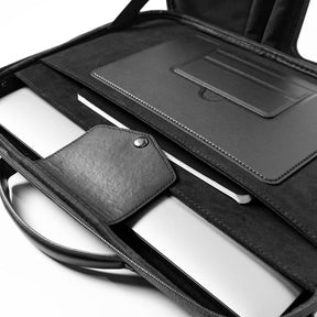 The interior of the portable briefcase shows a sleek black lining with a compartment for a laptop and a separate pocket for cards or documents, featuring a snap closure. A notebook is also visible beside the laptop, highlighting the organized layout.